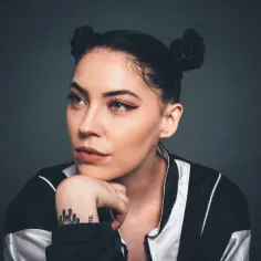 Portret Bishop Briggs z dwoma kokami na głowie, opierającej podbródek na dłoni.