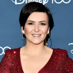 Katarzyna Łaska w błyszczącej czerwonej sukni, z kolczykami kołami. W tle logo Disney 100 i Polsat. "Mam tę moc"!