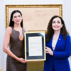 Dua Lipa, której dua lipa pochodzenie jest z Kosowa, odbiera dokument. Obok niej stoi kobieta w niebieskiej marynarce.