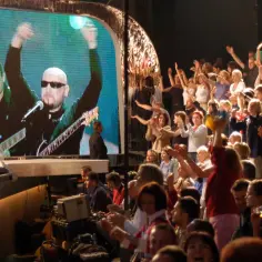 Koncertowy tłum szaleje, a na ekranie zespół grający "słodkiego miłego życia tekst".