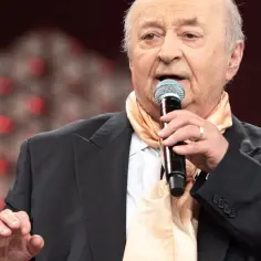 Bohdan Łazuka śpiewa, trzymając mikrofon. Jego charakterystyczne utwory rozbrzmiewają na scenie.