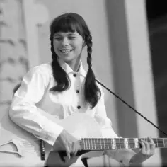 Karin Stanek z gitarą, uśmiechnięta, warkocze. Jej utwory niosą radość.
