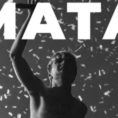 Mata z podniesioną ręką wśród konfetti, na tle napisu "MATA".