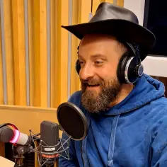 Łukasz Drapała w studio, w słuchawkach i kapeluszu, przygotowuje się do nagrania swoich utworów.