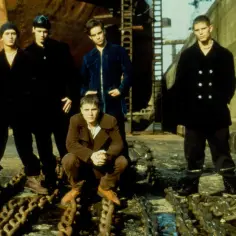 Mark Owen i koledzy z zespołu Take That pozują na tle stoczni.