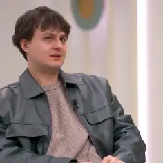 Młody mężczyzna w skórzanej kurtce i swetrze, wygląda na swój wiek.