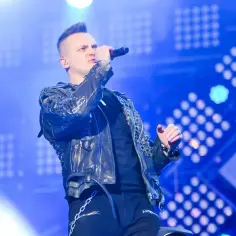 Nocny kochanek w skórzanej kurtce śpiewa na scenie, otoczony niebieskimi światłami.