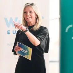 Kobieta w czarnej sukience przemawia, trzymając w ręku materiały z logo "Wind Europe".