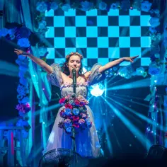 Sanah w kwiecistej sukni śpiewa na scenie, otoczona niebieskimi kwiatami i światłami. Koncert przypomina scenografię z jej albumów.
