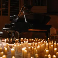 Nastrojowy koncert chopinowski przy blasku setek świec. Czarny fortepian i ławka dla pianisty na drewnianej scenie.