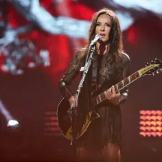 Kasia Kowalska na scenie, gra na gitarze i śpiewa. Jej stylizacja z frędzlami i siateczką idealnie pasuje do jej rockowego wizerunku.