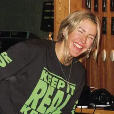 Uśmiechnięta Ellie Goulding w studiu, w koszulce z napisem "Keep it real". Jej utwory inspirują do autentyczności.