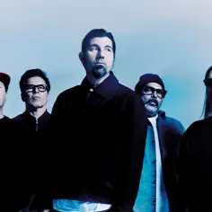 Pięciu mężczyzn z zespołu Deftones, znanych z kultowych **Deftones albumy**, pozuje na tle błękitnego nieba.