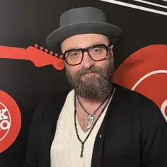 Mężczyzna w kapeluszu i okularach, z brodą, przed ścianką z logo Rock Radio. Tekst "perfect wszystko ma swój czas" idealnie pasuje do tej chwili.