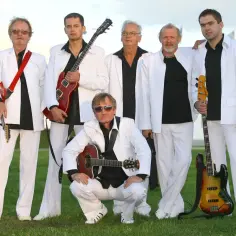 Zespół w białych garniturach, z czerwonymi gitarami i basem, gotowy do koncertu.