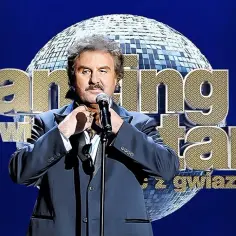 Krzysztof Krawczyk w garniturze, z mikrofonem, na tle kuli dyskotekowej i napisu "Dancing with the Stars". Jego przeboje rozbrzmiewały na parkiecie.
