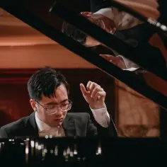 Młody pianista w okularach, skupiony na grze, przygotowuje się do występu na konkursie chopinowskim 2025.