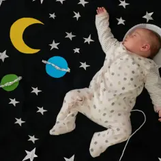 Śpiące dziecko w piżamce z kropkami, jak mały astronauta, wśród gwiazd i planet. Ach, śpij kochanie, tekst kołysanki idealnie pasuje.