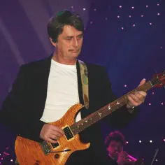 Muzyk grający na gitarze, przypominający styl Mike'a Oldfielda. Koncertowa atmosfera z fioletowym tłem i świetlnymi akcentami.