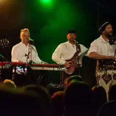 Baciary grają, a w tle siedem czerwonych róż. Muzycy w białych koszulach i góralskich spodniach na scenie.