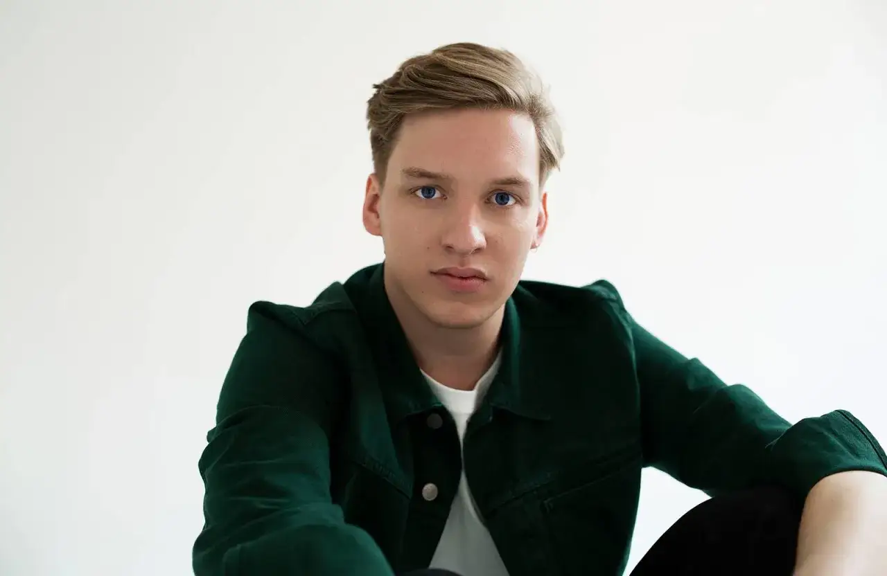George Ezra w zielonej kurtce, z błękitnymi oczami, jakby śpiewał 