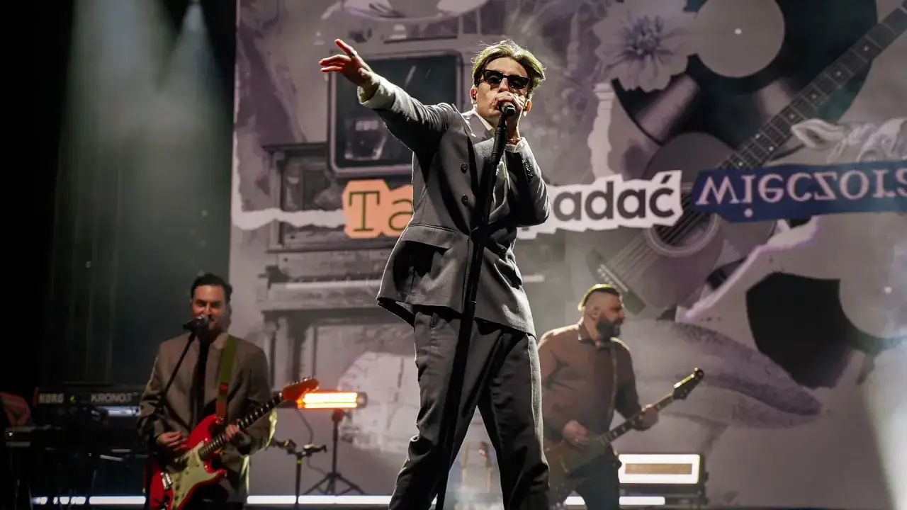 Dawid Kwiatkowski w garniturze na scenie, z mikrofonem w dłoni. Jego wzrost robi wrażenie, gdy śpiewa dla publiczności.