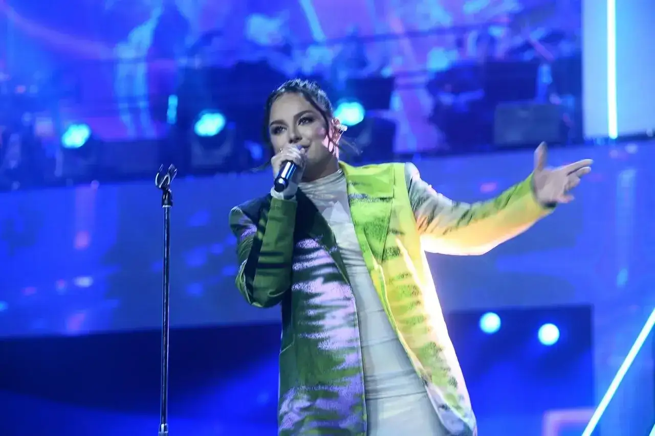Ewa Farna śpiewa na scenie w kolorowej marynarce. Fani szukają jej piosenki alfabetycznie.