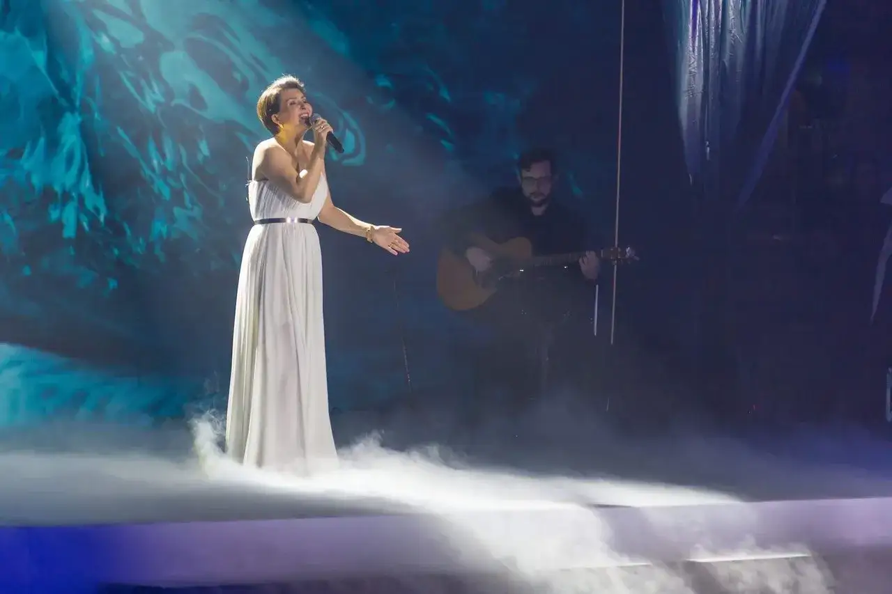 Katarzyna Łaska śpiewa na scenie, otoczona mgłą. W tle mężczyzna gra na gitarze. 