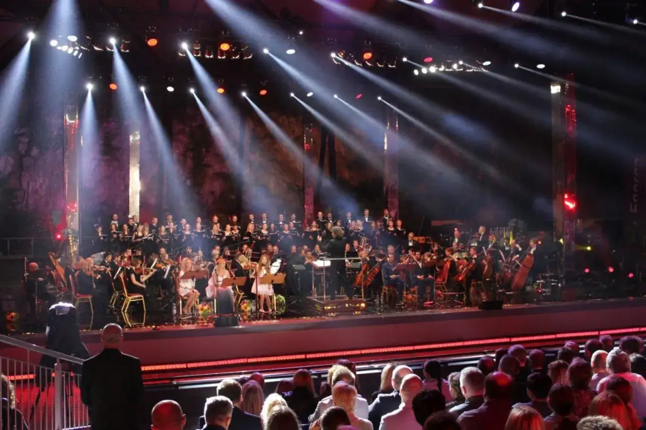 Koncert Piotra Rubika z orkiestrą i chórem, światła sceniczne tworzą magiczną atmosferę.