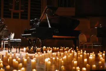 Nastrojowy koncert chopinowski przy blasku setek świec. Czarny fortepian i ławka dla pianisty na drewnianej scenie.