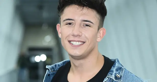 Uśmiechnięty Dawid Kwiatkowski w dżinsowej kurtce. Jego wzrost jest typowy dla młodego mężczyzny.