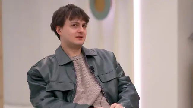 Młody mężczyzna w skórzanej kurtce i swetrze, wygląda na swój wiek.